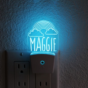 May include: A white night light with a blue light that illuminates a rainbow and clouds with the name Maggie.