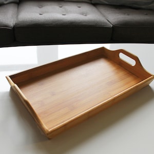 May include: A rectangular wooden serving tray with two handles. The tray is made of light brown bamboo and has a smooth, polished finish.