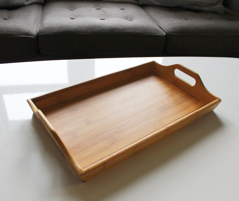 May include: A rectangular wooden serving tray with two handles. The tray is made of light brown bamboo and has a smooth, polished finish.