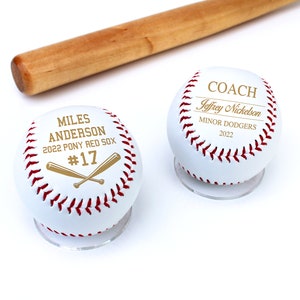 May include: Two white baseballs with gold lettering on a white background. One baseball says "Miles Anderson 2022 Pony Red Sox #17" with two crossed bats. The other baseball says "Coach Jeffrey Nickleson Minor Dodgers 2022".