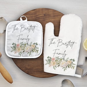 May include: A set of two white kitchen pot holders with floral designs and the text "The Bartlett Family".