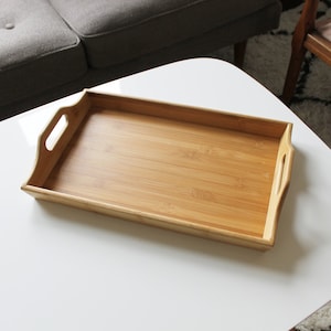 May include: A rectangular wooden serving tray with two handles on the sides. The tray is made of light brown bamboo and has a smooth surface.
