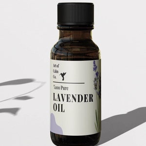 Może przedstawiać: Mała brązowa butelka ze szkła z czarną zakrętką i białą etykietą. Etykieta zawiera napis "Art of Calm Co." i "100 Pure Lavender Oil". Na etykiecie znajduje się mała ilustracja kolibra.