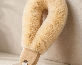 May include: A U-shaped body brush with light beige natural bristles and a smooth, light-toned wooden handle. The brush features a small, white fabric loop attached to the base of the handle for convenient hanging and storage purposes.