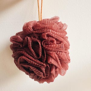 Può includere: Primo piano di un  puf per il bagno rosa con uno spago giallo attaccato.