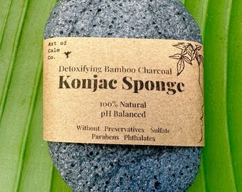 May include: A black charcoal konjac sponge with a brown paper label that reads "Detoxifying Bamboo Charcoal Konjac Sponge 100% Natural pH Balanced Without Preservatives Sulfate Parabens Phthalates".