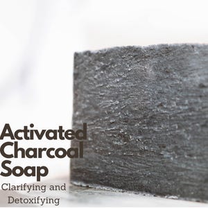May include: A close-up of a gray, rectangular bar of soap. The soap is labeled 'Activated Charcoal Soap' and 'Clarifying and Detoxifying'.
