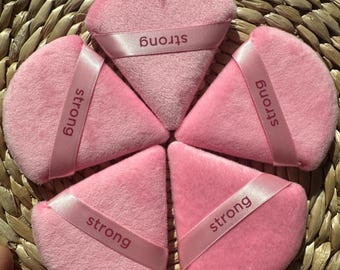 May include: Five pink triangular makeup sponges with a pink ribbon around each one that says "strong" in white lettering.