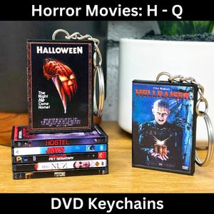 Puede incluir: Llaveros de DVD con portadas de películas de terror, incluyendo "Halloween" y "Hellraiser". El llavero de "Halloween" muestra una calabaza con un cuchillo. Otros llaveros incluyen "Hostel", "Jaws" y "Pet Sematary". El texto "Horror Movies: H - Q" y "DVD Keychains" son visibles.