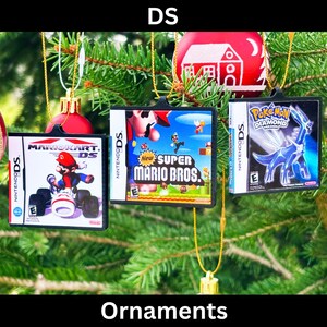 Puede incluir: Adornos navideños con forma de cajas de juegos de Nintendo DS. Los adornos incluyen Mario Kart DS, New Super Mario Bros. y Pokémon Diamante. Cuelgan de hilos dorados, con otras bolas navideñas en el fondo.