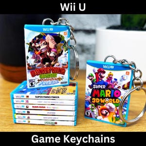 May include: Keychains featuring miniature Wii U game cases. One keychain displays "Super Mario 3D World" artwork, while others showcase "Donkey Kong Country: Tropical Freeze" and other game titles. The text "Game Keychains" is at the bottom.