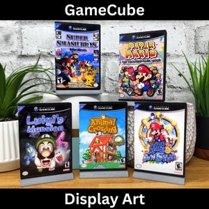 May include: Five GameCube video game cases with colorful artwork. The games are Super Smash Bros. Melee, Paper Mario: The Thousand-Year Door, Luigi's Mansion, Animal Crossing, and Wario World.