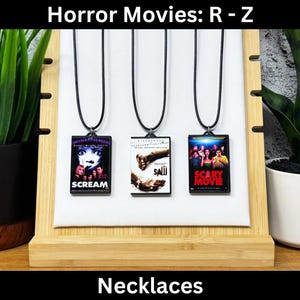 May include: Three black necklaces with movie themed pendants. The pendants feature images from the films "Scream", "Saw", and "Scary Movie".