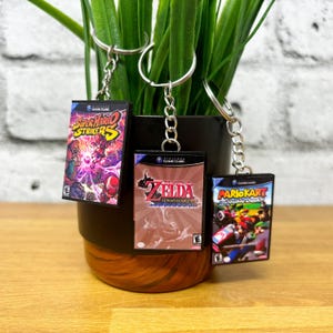 May include: Three miniature GameCube game cases on keychains. The cases are for Super Mario Strikers, The Legend of Zelda: The Wind Waker, and Mario Kart: Double Dash!!