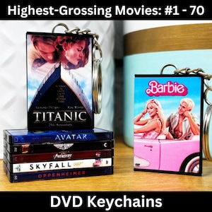 May include: Two DVD keychain sets featuring the highest-grossing movies. The first set features a black keychain with a Titanic movie poster and a stack of DVDs with the titles Avatar, Top Gun: Maverick, Avengers: Endgame, Skyfall, and Oppenheimer. The second set features a black keychain with a Barbie movie poster.