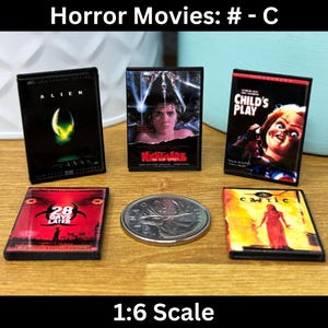 Puede incluir: Una colección de seis cintas VHS de películas de terror en miniatura, incluyendo Alien, Pesadilla en Elm Street, Juego de niños, 28 días después, Carrie y una sexta cinta con un título borroso. Las cintas están dispuestas en dos filas de tres sobre una superficie de madera.