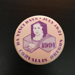 May include: A round, light pink button with purple text and graphics. The button features an image of the Mona Lisa and the text "DA VINCI DAYS JULY 19-21 CORVALLIS OREGON 1991".