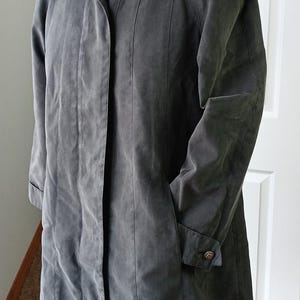 May include: A long, dark gray coat with a collar and button closure. The coat has long sleeves, pockets, and a button detail on the cuff. The coat is displayed on a mannequin.