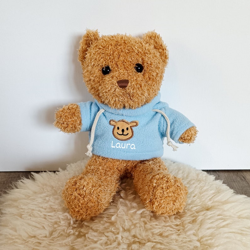 Der blaue Sweater ist mit Name und einem kleinen Teddy versehen