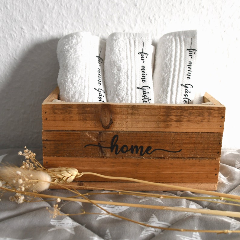 Holz-Box mit Handtüchern in weiß. Die Schrift Schön dass du da bist und Home wird passend zu den Handtüchern in Schwarz gedruckt. Ein tolles Geschenk zum Einzug