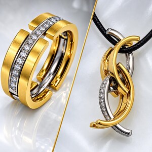 May include: A gold and silver-coloured ring featuring a central channel set with small clear stones, alongside a pendant on a black cord composed of interlocking gold and silver-coloured curved metal pieces, with one section accented by clear stones.