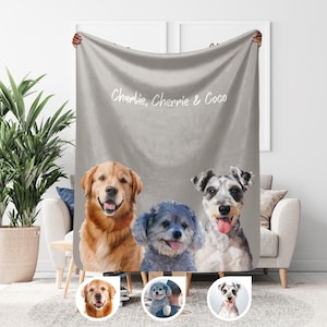 May include: A gray blanket featuring a watercolor painting of three dogs: a golden retriever, a blue-gray poodle mix, and a gray and white schnauzer. The blanket has the text "Charlie, Cherrie & Coco" in white script.