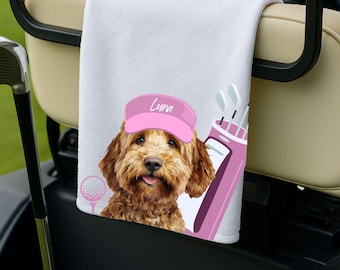 Puede incluir: Toalla de golf blanca con un perro de dibujos animados que lleva una visera rosa con el nombre "Luna". La toalla también muestra una bolsa de golf rosa, una pelota de golf y un palo de golf. La toalla está colgada en un carrito de golf.