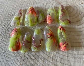 Peut inclure: Dix faux ongles verts et transparents avec un motif floral et des accents de paillettes.
