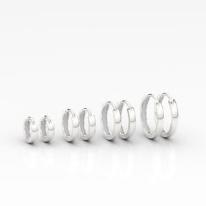 May include: Six pairs of silver hoop earrings in different sizes are displayed. The earrings are arranged in a row, each pair with a polished, reflective surface. The hoops are a simple, classic design, suitable for everyday wear.
