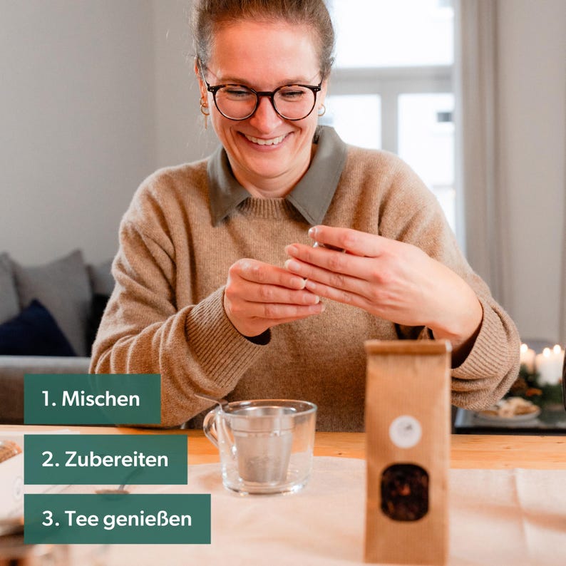 May include: A woman smiles as she holds a brown tea bag package. Three green rectangular boxes with white text are on the table: "1. Mix", "2. Prepare", and "3. Enjoy Tea".