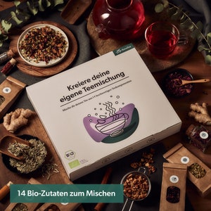 May include: A white box with the text "Kreiere deine eigene Teemischung" and "Mische dir deinen Tee aus 14 hochwertigen Teekomponenten". The box is surrounded by various tea ingredients, including dried flowers, herbs, and spices. The box is labeled "Bonates" and features a green and purple illustration of a teacup.