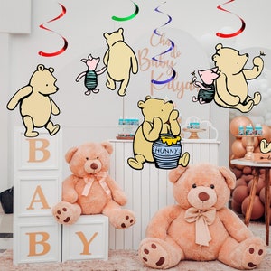 May include: A Winnie the Pooh themed baby shower decoration set with Winnie the Pooh and Piglet characters,  a honey pot, and a 'Baby' block set. The decorations are hanging from the ceiling with red, green, and blue curly streamers.