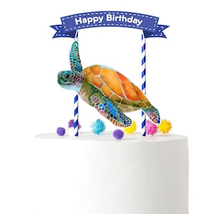 May include: A cake topper featuring a colorful sea turtle with a blue banner that reads "Happy Birthday". The turtle is on two blue and white striped sticks. The cake topper is surrounded by colorful pom-poms.