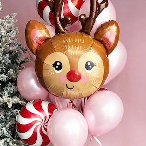 May include: A festive balloon bouquet featuring a reindeer-shaped balloon with brown antlers, a red nose, and a smiling face. The bouquet includes pink and red and white swirl balloons, and other pink balloons. A red ribbon ties the balloons together.