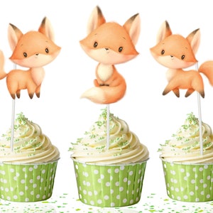 May include: Three cupcakes with green and white polka dot liners topped with white frosting and green sprinkles. Each cupcake has a fox topper with orange fur and a white tail.