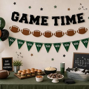 May include: A football-themed party display featuring a GAME TIME banner, brown football cutouts, and green yard-line pennants. The table includes sliders, popcorn, pretzels, a metal tub with drinks, and signs reading EAT. DRINK. FOOTBALL.