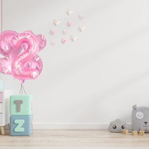 May include: Pink number two balloons with butterfly accents, a set of alphabet blocks spelling "T" and "Z", and a white giraffe stuffed animal with brown spots.