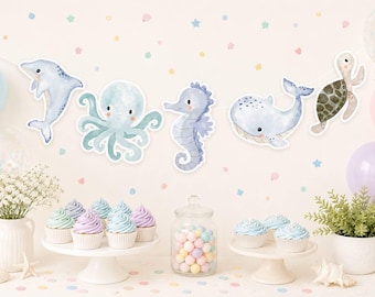 May include: A decorative garland featuring watercolor-style illustrations of a dolphin, octopus, seahorse, whale, and sea turtle. The sea creatures are rendered in soft blue and green tones with white outlines, suspended horizontally against a wall.