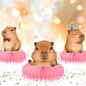 May include: Three adorable capybaras are featured, each perched on a pink honeycomb decoration. One wears a bow tie, another a party hat, and the third waves. The background includes blurred candles and confetti, suggesting a birthday theme.