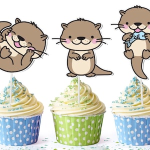 May include: Three cupcake toppers featuring cartoon otter illustrations. The otters are brown with pink cheeks and are in different poses. The toppers are on top of cupcakes with white frosting and blue, green, and white sprinkles.