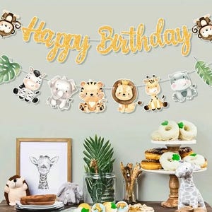 May include: A gold glitter "Happy Birthday" banner with cartoon animal decorations, including a zebra, elephant, tiger, lion, giraffe, and hippo. The image also features a framed giraffe print and a tiered dessert stand with doughnuts.