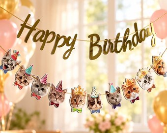 May include: A gold-colored banner with the text Happy Birthday in cursive script, strung above a garland featuring multiple cutouts of cat faces wearing colorful party hats and bow ties, suspended against a blurred background.