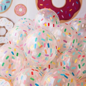 May include: Clear balloons decorated with colorful sprinkles, clustered together. The background features donut-shaped decorations in various colors, creating a festive and playful atmosphere. Ideal for a birthday party or celebration.