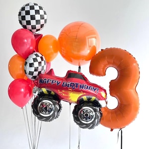 May include: A festive balloon arrangement for a birthday celebration. It features a red monster truck balloon with "HAPPY BIRTHDAY!" text, an orange number 3 balloon, and various red, orange, and checkered balloons.