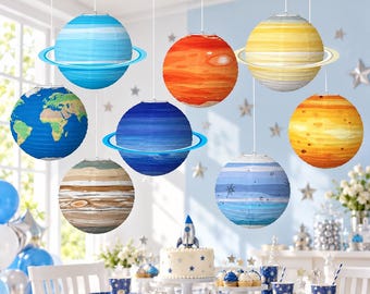 May include: A set of eight spherical paper lanterns designed to resemble planets in the solar system, including Earth, Saturn, and Jupiter, suspended from the ceiling with white strings to create a space-themed display for a party.
