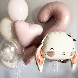 May include: A pink number two balloon, a pink heart balloon, a white bunny balloon with pink ears, and a clear balloon with gold glitter inside. There are also several white balloons in the background.