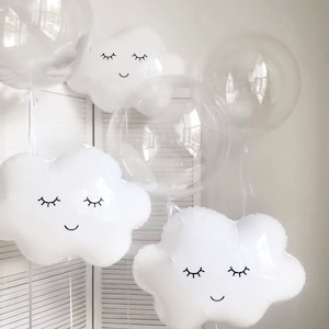 May include: White cloud-shaped balloons with black sleepy eyes and smiling mouths. The balloons are tied together and floating in the air.