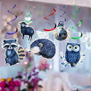 May include: A collection of hanging woodland animal decorations, including a raccoon, sheep, hedgehog, fox, and owl. Each animal is a deep blue color with gold star accents. Colorful streamers and confetti add a festive touch to the party decorations.