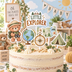 Peut inclure: Un ensemble de décorations de gâteau comprenant un ours avec un chapeau de safari, un globe, une boussole, une carte, une tente et un panneau indiquant Little Explorer. Les décorations sont disposées sur un gâteau au glaçage blanc.