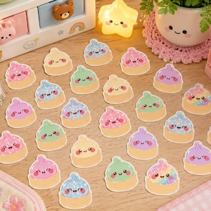May include: A collection of die-cut stickers featuring various colorful soup dumplings with smiling faces. The dumplings are depicted in shades of pink, blue, green, purple, and yellow, some with glittery or holographic textures, arranged on a surface.